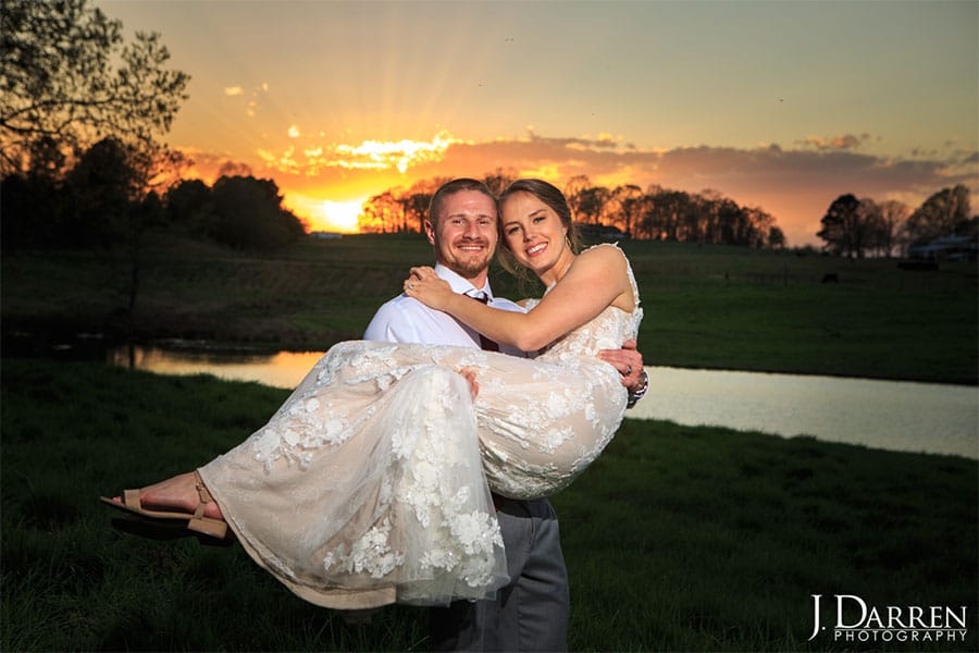 The groom is holding the bride while the sun is setting in the background.
