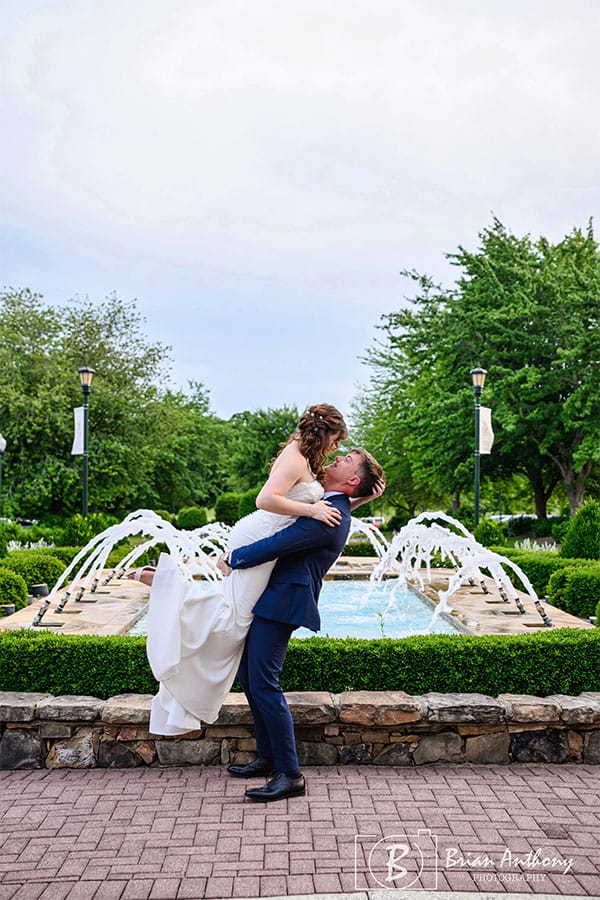 The groom holding the bride in front of a fountain.