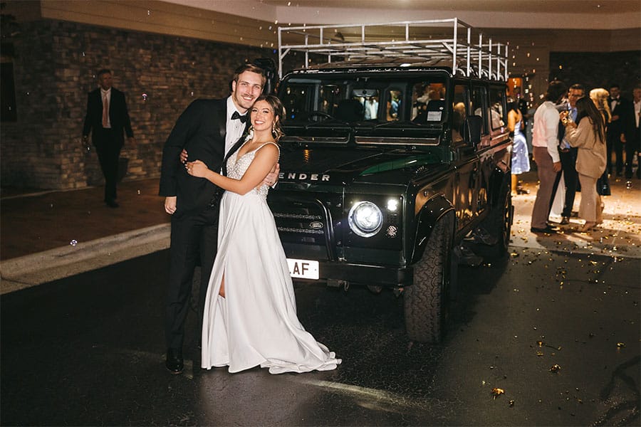 The bride and groom in front of a car.