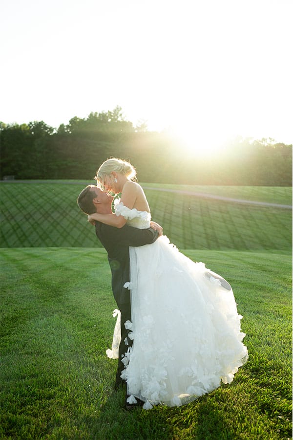 The groom picking up the bride in a field.