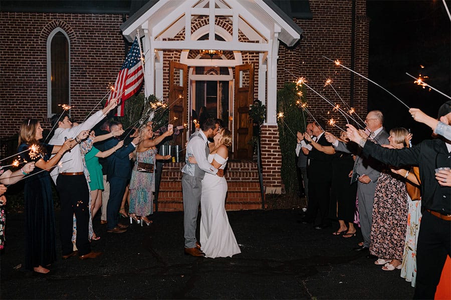 The bride and groom kissing with sparklers around them.