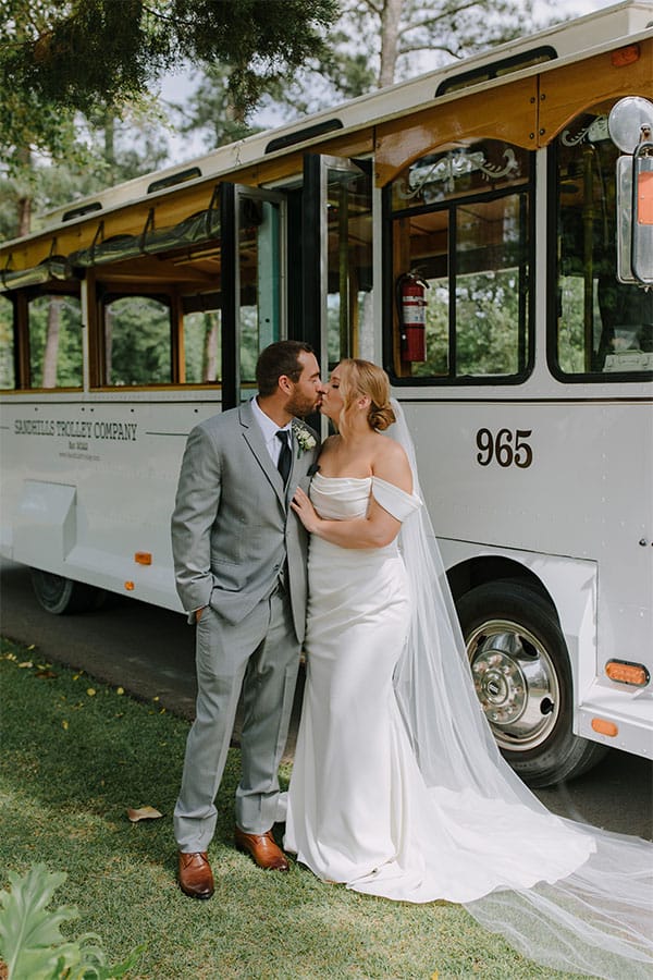 The bride and groom kissing in front of a bus.