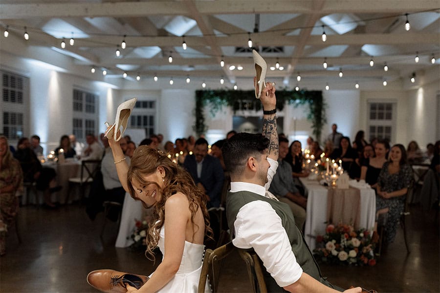 The bride and groom sitting back to back holding a shoe up.