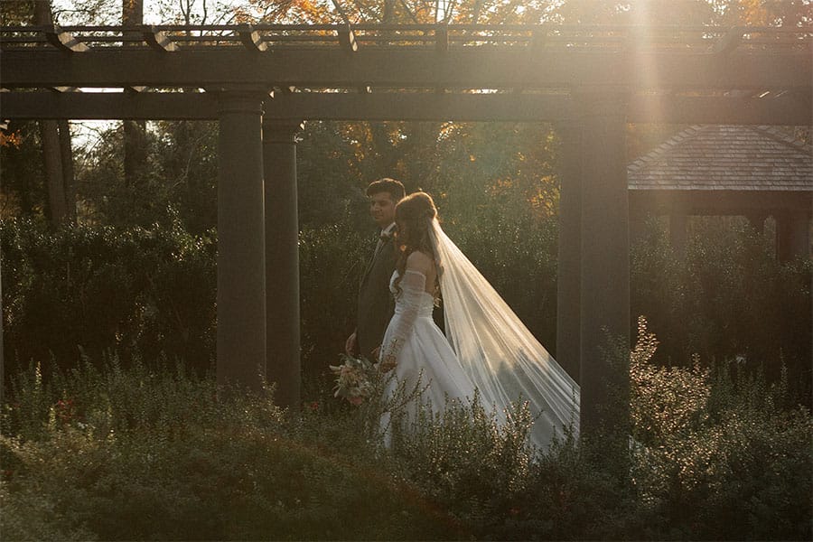 The bride and groom walking through a garden.