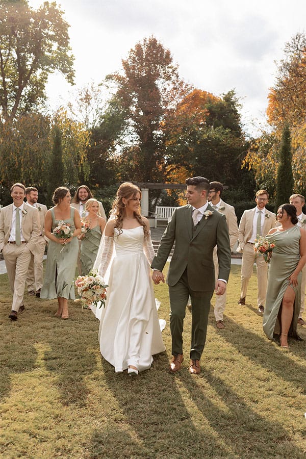 The bride and groom holding hands with their bridesmaids and groomsmen behind them.