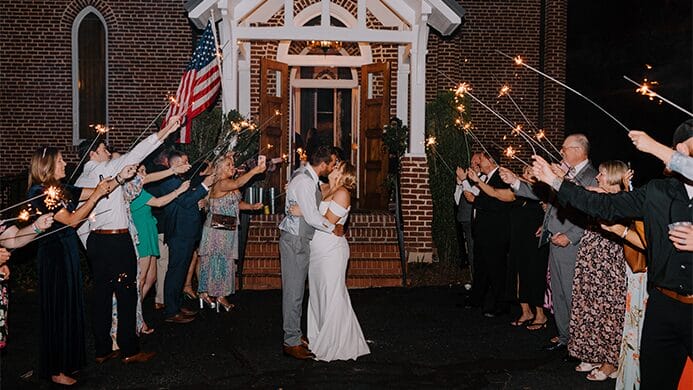 The bride and groom kissing with sparklers around them.